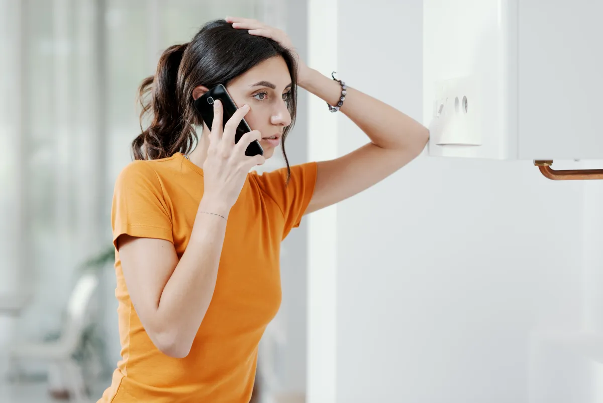 Woman on phone looking worriedly at a boiler or water heater